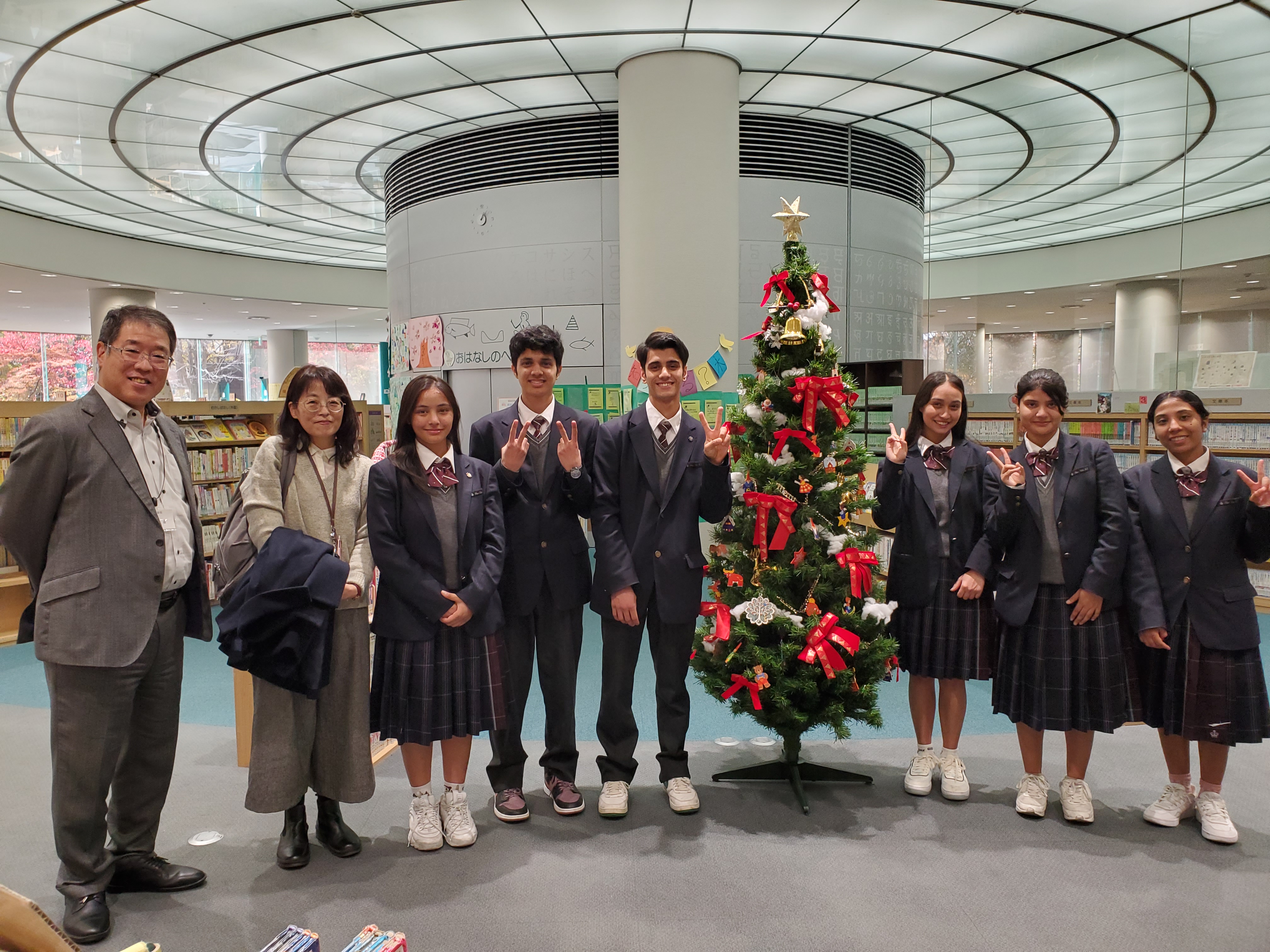 クリスマスツリーの前で撮った大阪府立布施北高校の生徒6人と先生、当館館長との8人での記念写真