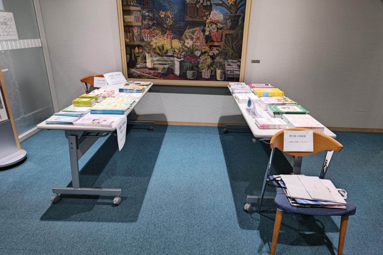 長机2台の上に出版社の図書カタログを並べている 手前の椅子には持ち帰り用の紙袋がおかれている。