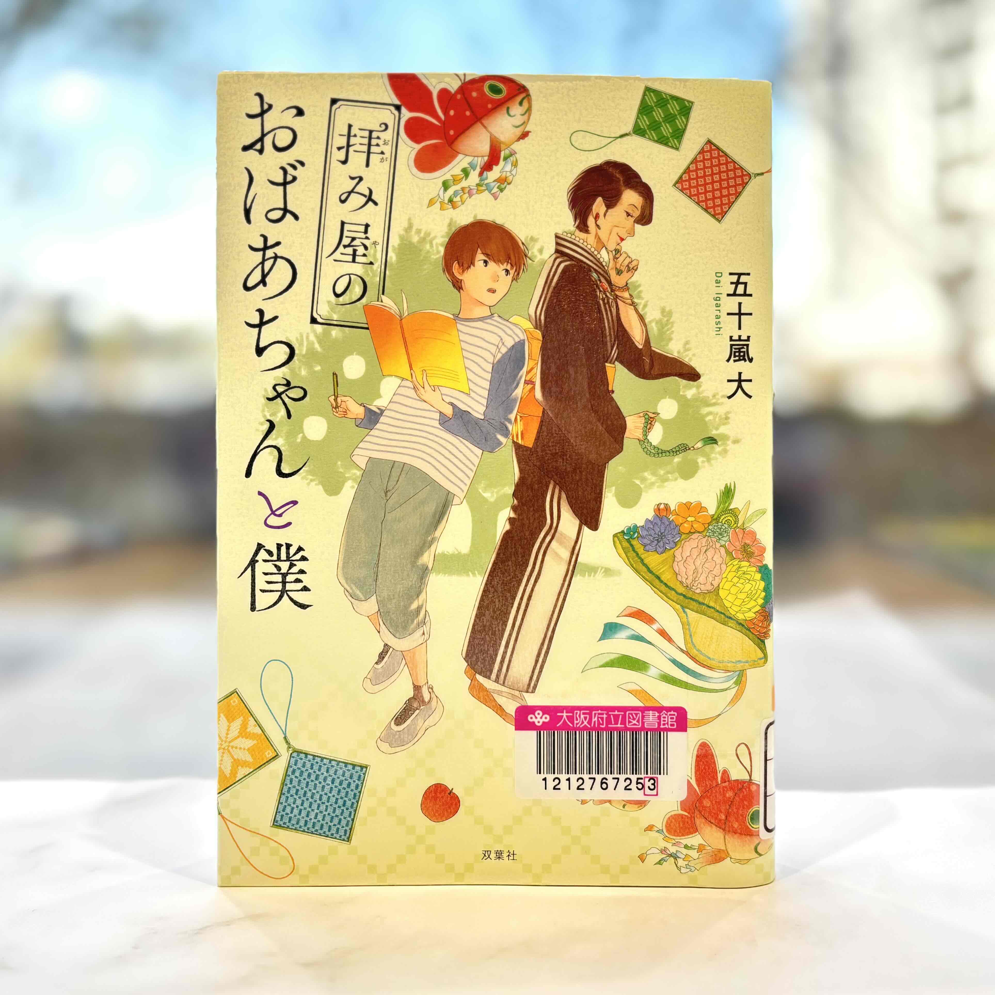 『拝み屋のおばあちゃんと僕』の表紙画像。本を持つ男の子の背後に、顎に手を添えて考えるポーズをとる和服姿の女性が立っているイラスト。