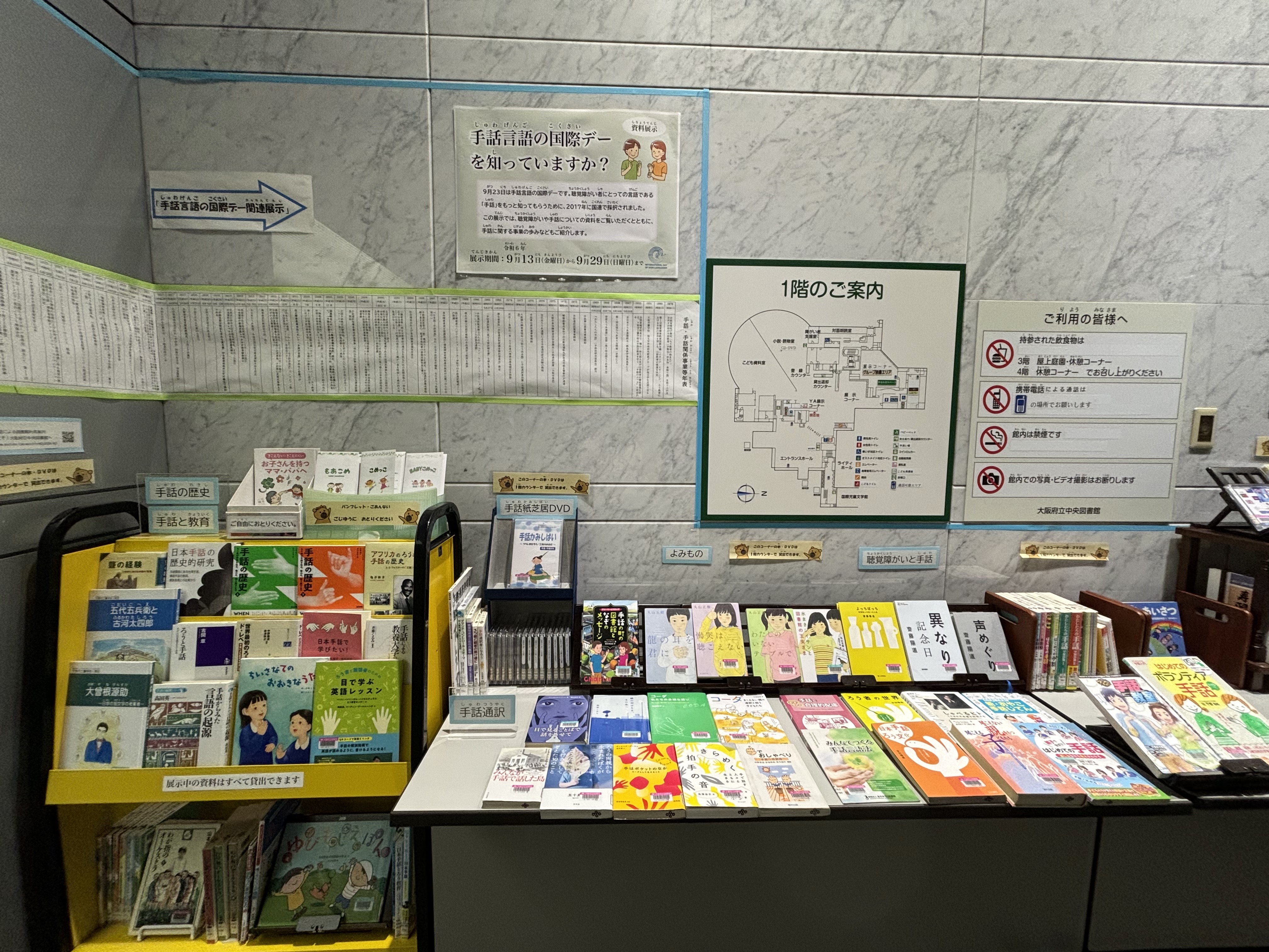 資料展示「手話言語の国際デーを知っていますか？」の展示風景写真。展示見出しの下に年表、その下、左手には本をのせる展示台に表紙を見せて本が並んでいる。その右側に机の上にも表紙を見せた本やDVDが並んでいる。