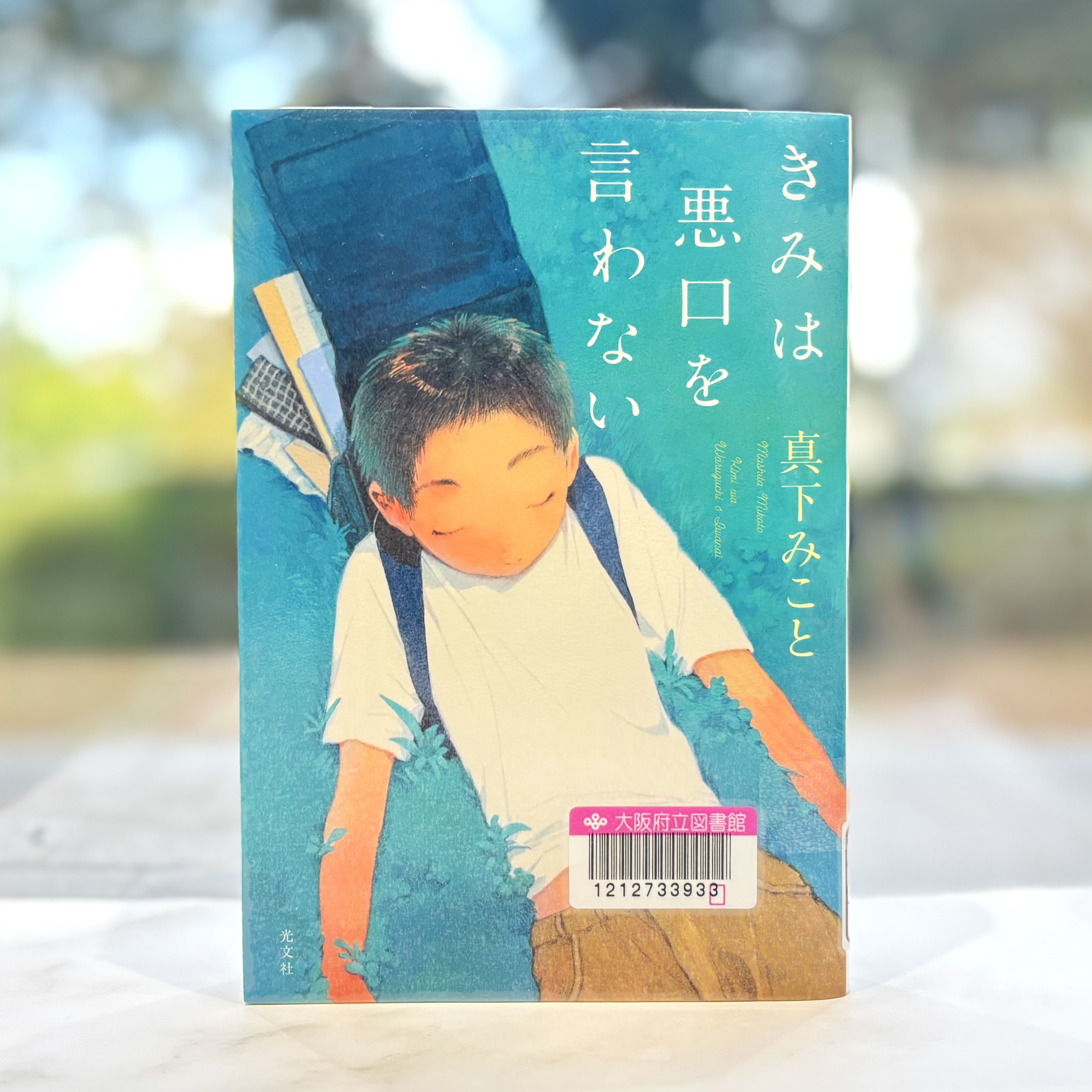 『きみは悪口を言わない』の表紙画像。ランドセルを背負った男の子が芝生の上に寝転がっているイラストが描かれている。