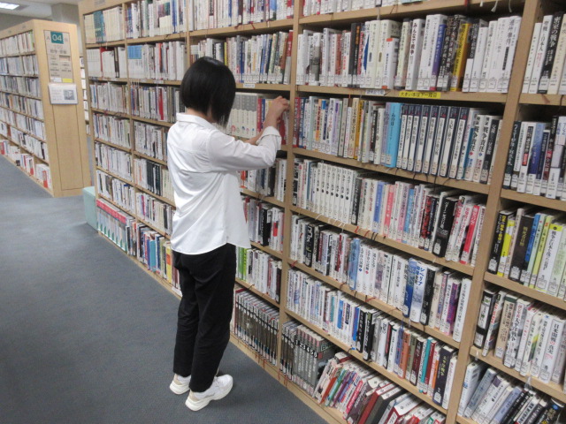 インターンシップの学生が書架で本の並びを整理している様子。