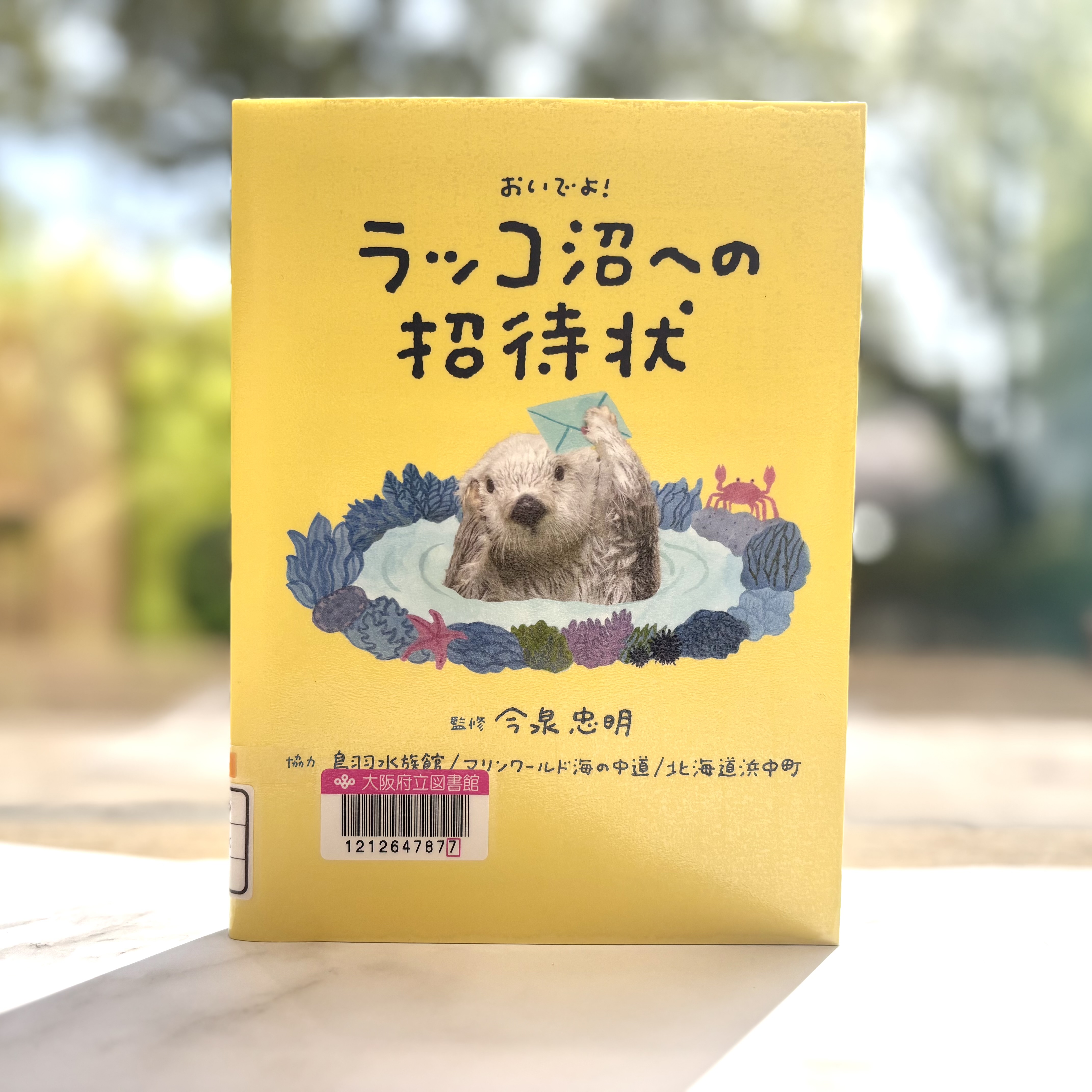 『おいでよ!ラッコ沼への招待状』の表紙画像。黄色い背景の真ん中にラッコが温泉に入っているイラスト。