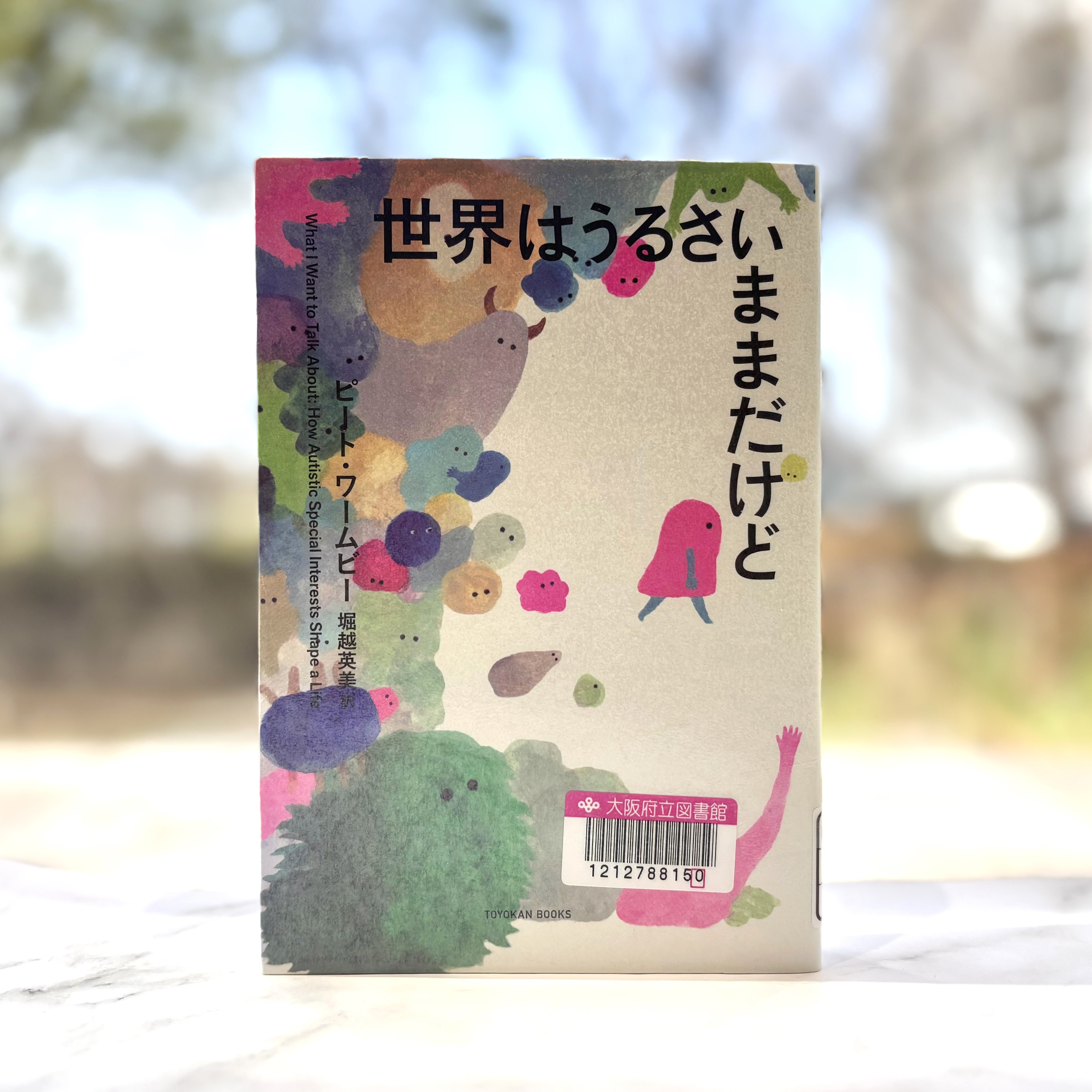 『世界はうるさいままだけど』の表紙画像。カラフルで不思議な形の生き物たちが集まっている中に、ピンク色のキャラクターが歩いているパステル調のイラスト。