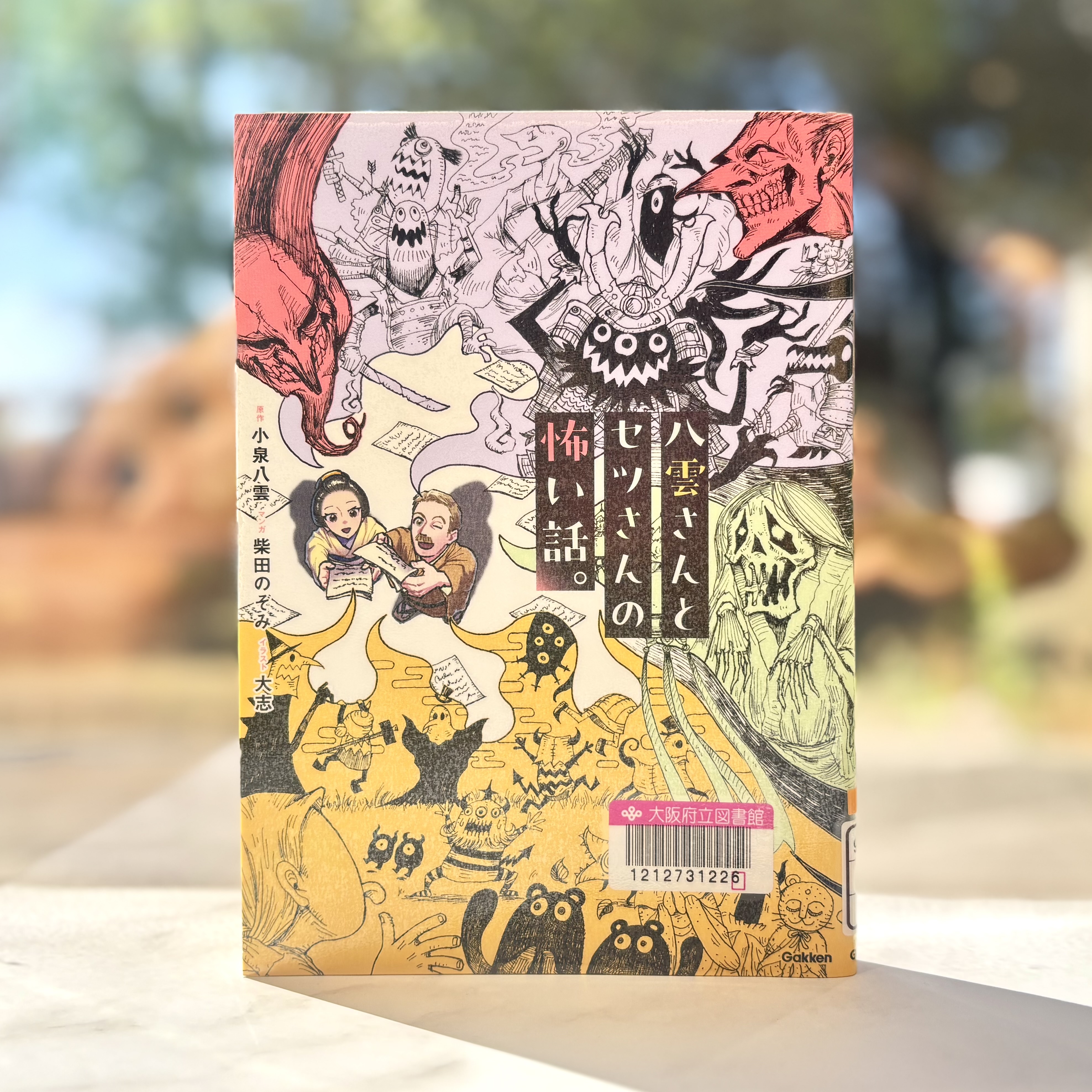 『八雲さんとセツさんの怖い話。』の表紙画像。八雲さんとセツさんが持っている紙からいろいろな妖怪が飛び出しているイラストが描かれている。