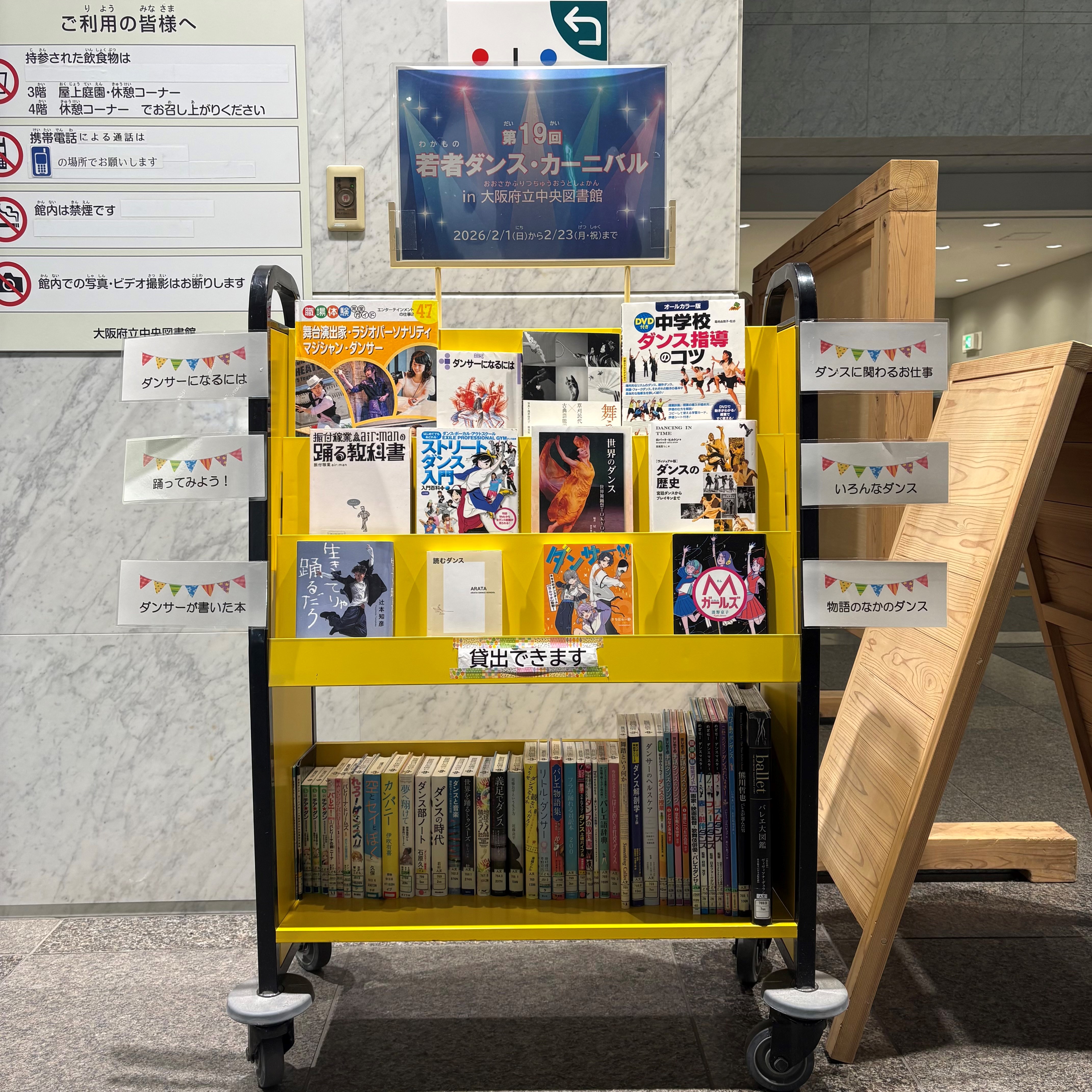 「第19回若者ダンス・カーニバル in 大阪府立中央図書館」の展示風景写真。展示見出しのついたブックトラックに本が上3段に表紙を見せた状態で並び、1番下は背表紙が見える向きで本が並んでいる。