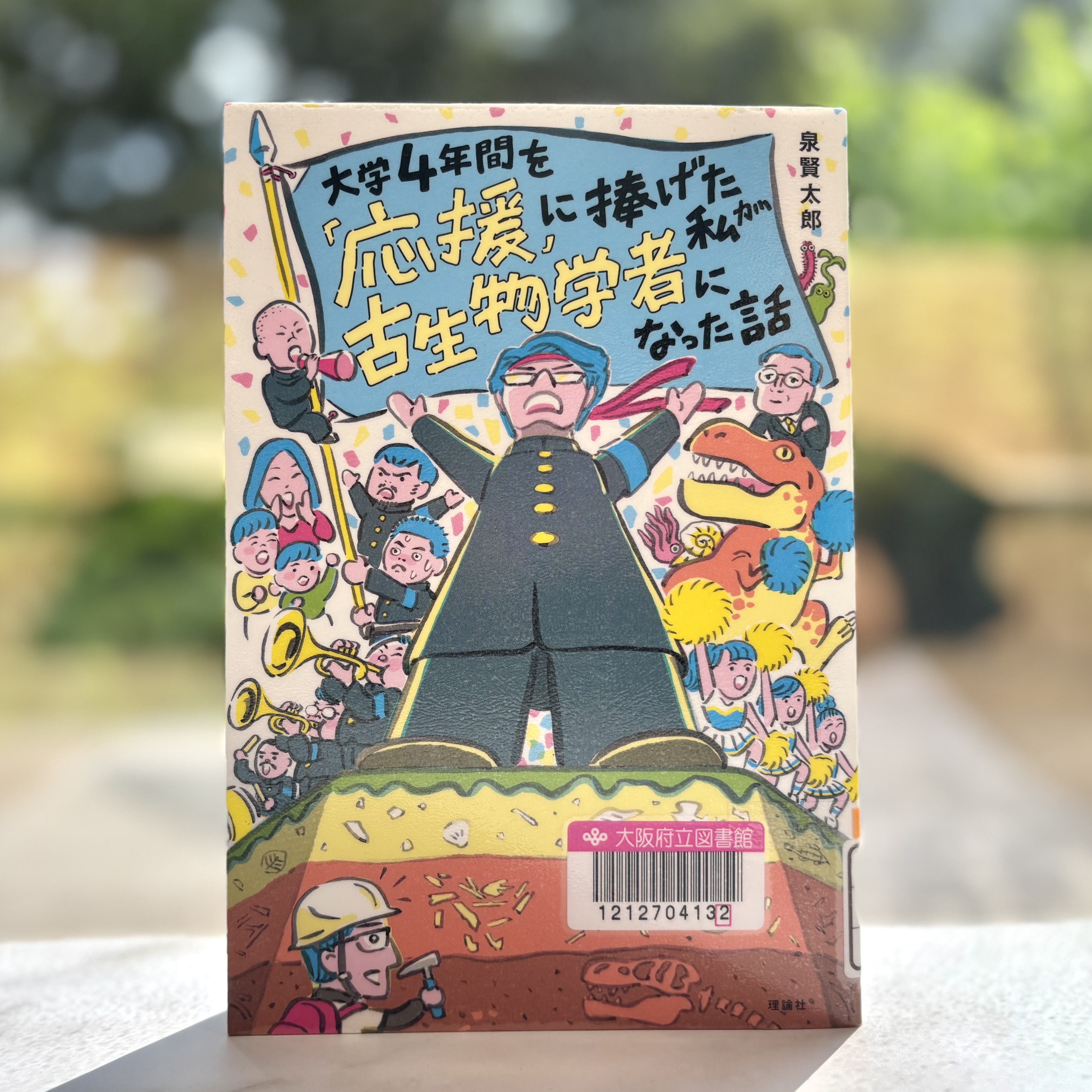 『大学4年間を「応援」に捧げた私が古生物学者になった話（世界をカエル　10代からの羅針盤）』の表紙画像。応援団の格好をした男性の後ろで旗が立っており、タイトルが書かれているイラスト。