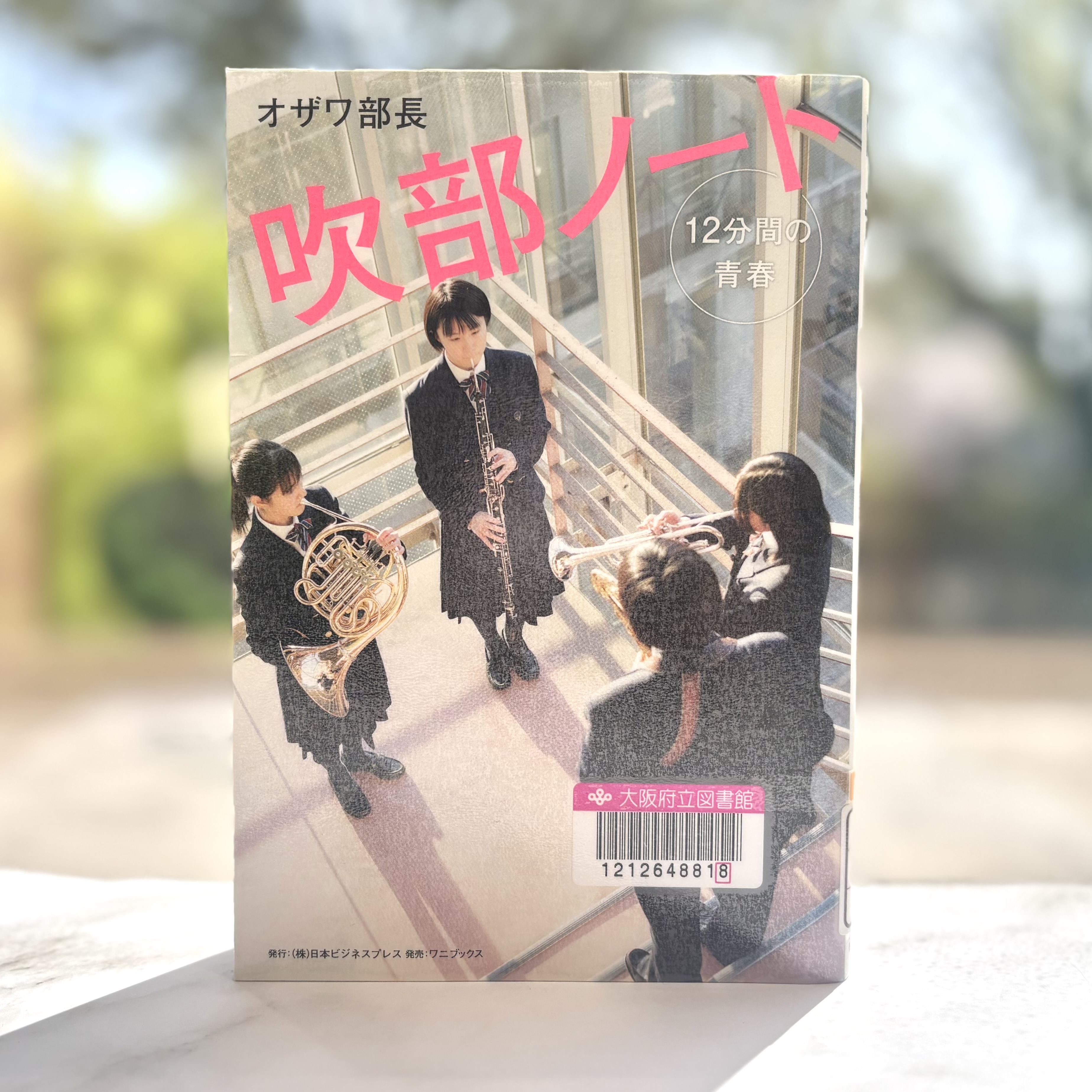 『吹部ノート：12分間の青春』の表紙画像。三人の女生徒が向かい合って楽器を演奏している。