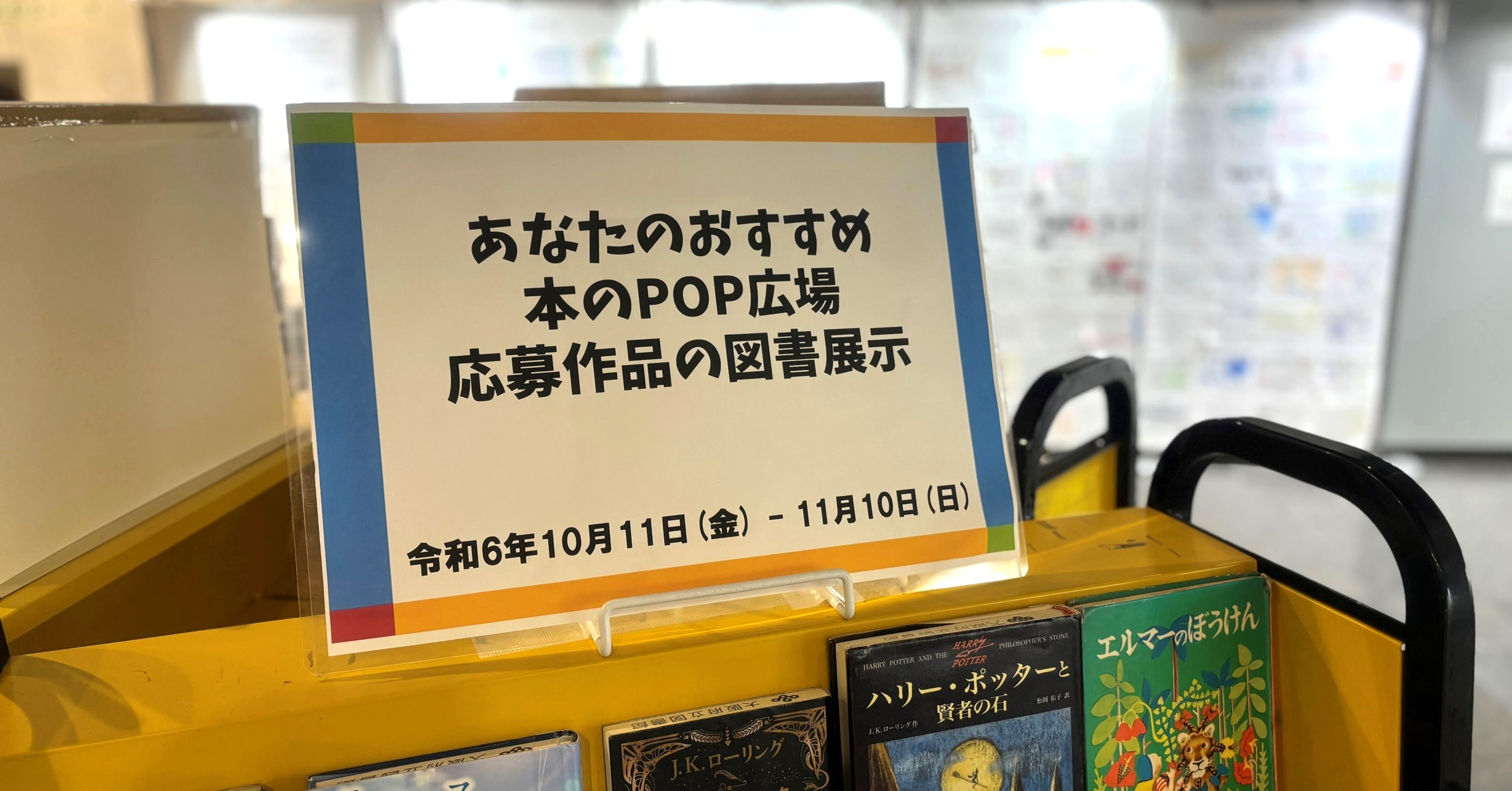 ブックトラックの上に掲示された「あなたのおすすめ本のPOP広場応募作品の図書展示」と書かれた案内