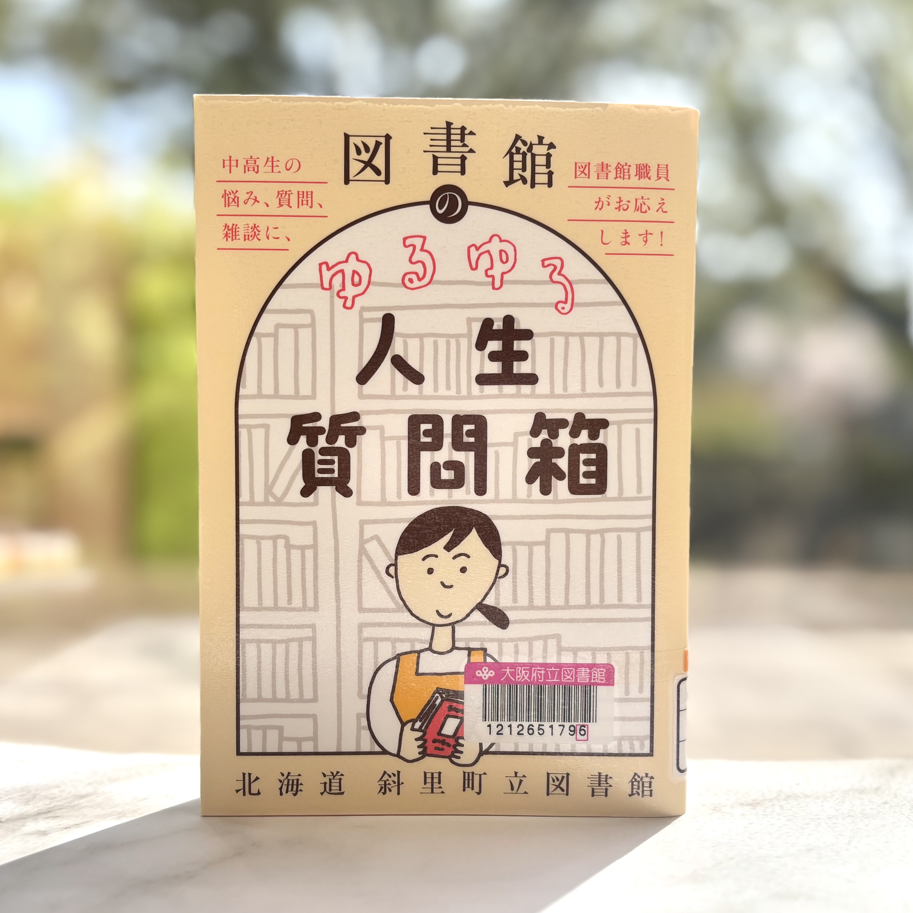 『図書館のゆるゆる人生質問箱：中高生の悩み、質問、雑談に、図書館職員がお応えします!』の表紙画像。本棚を背にして本を手にもつ笑顔の女性のイラスト。