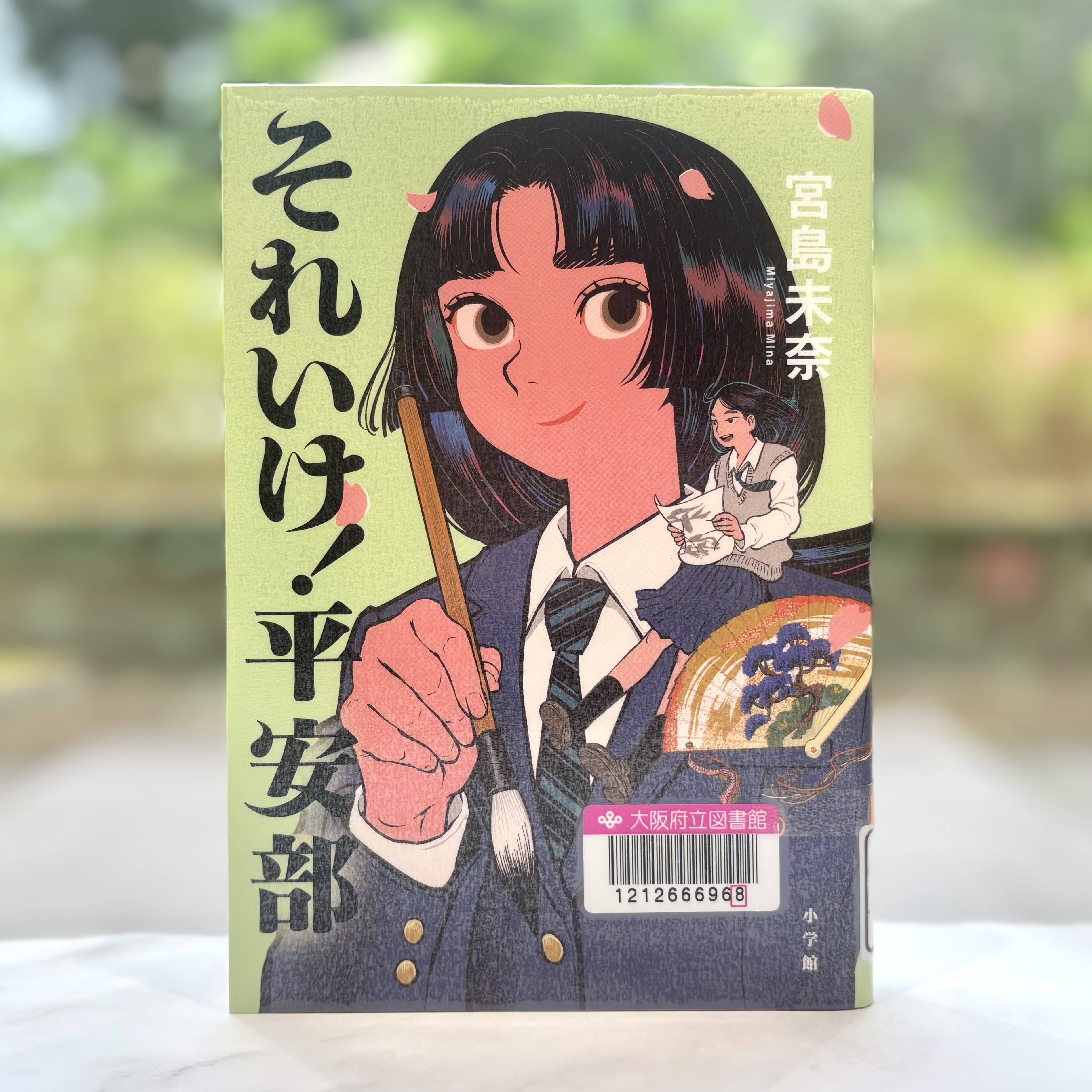 『それいけ!平安部』の表紙画像。黄緑色の背景の真ん中に筆を持った女子高生がいるイラスト。