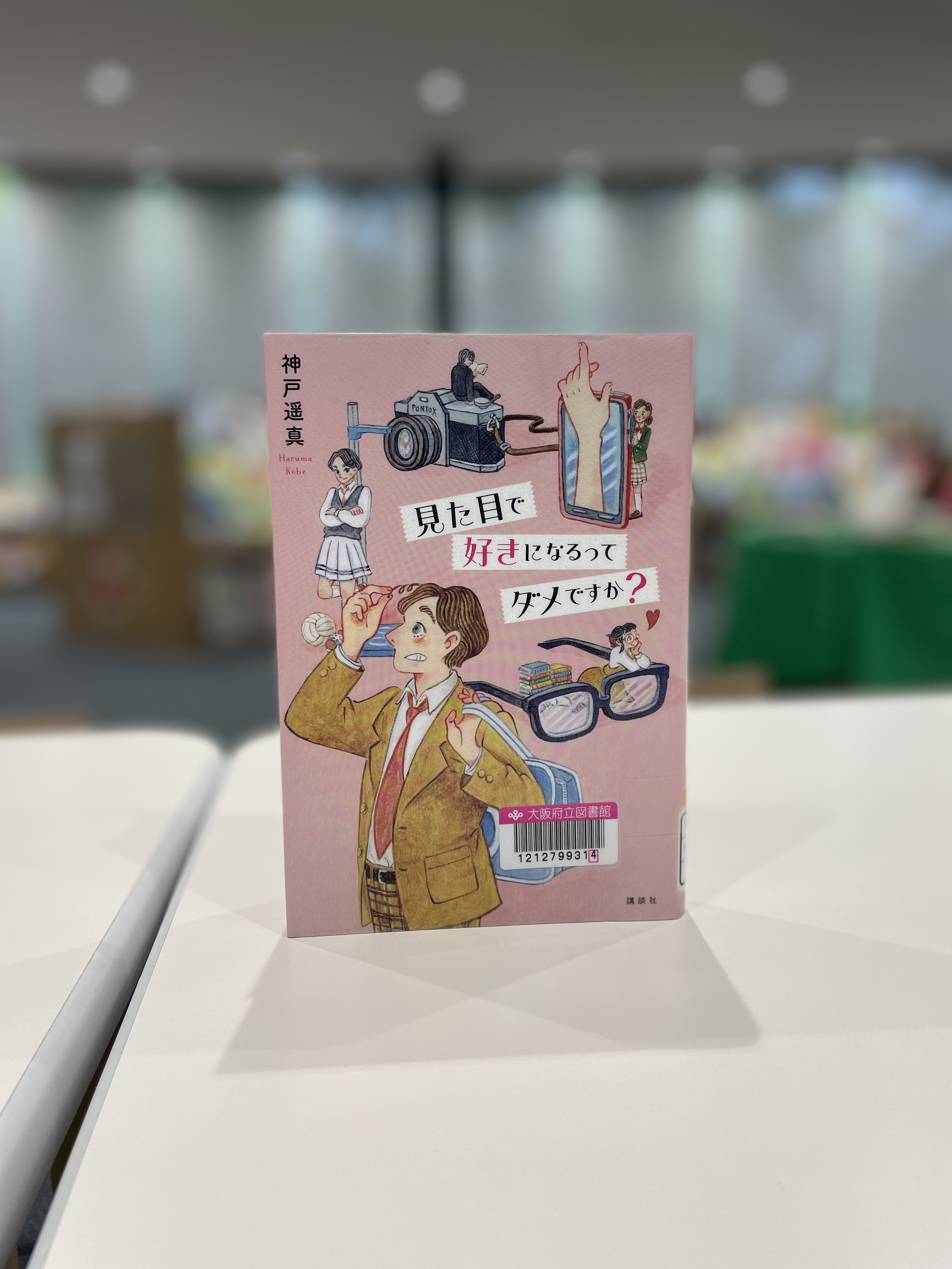 『見た目で好きになるってだめですか？』の表紙画像。ピンク色の背景に高校生5人とスマホ、メガネ、カメラ、身長計のイラストが描かれている。