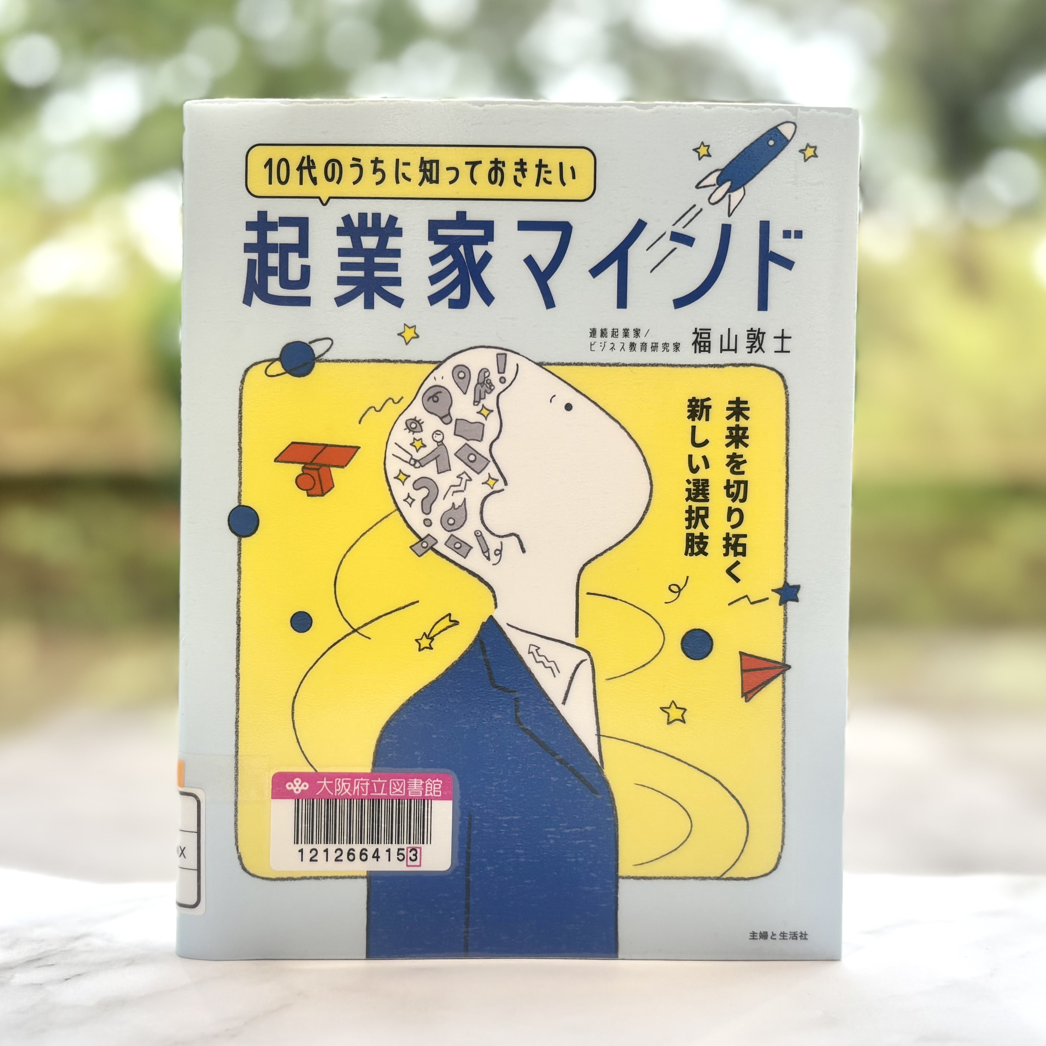 『10代のうちに知っておきたい起業家マインド：未来を切り拓く新しい選択肢』の表紙画像。タイトルの下に、黄色い背景に青い服を着た男の人が上を向いた右上半身の絵。