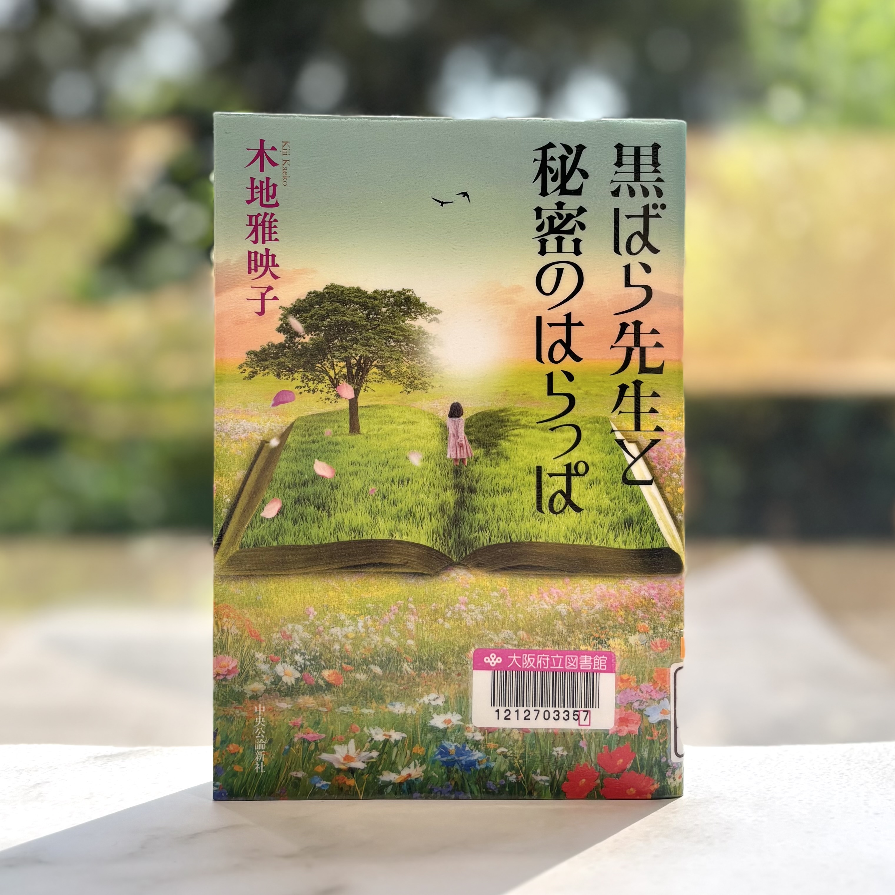 『黒ばら先生と秘密のはらっぱ』の表紙画像。草原の中に大きな本が開かれ、真ん中に女の子が後ろを向いて立っているイラスト。