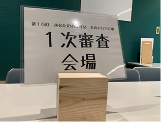 1次審査会場案内掲示:四角い木のブロックの真ん中の切り目に案内掲示の紙がはさまっている